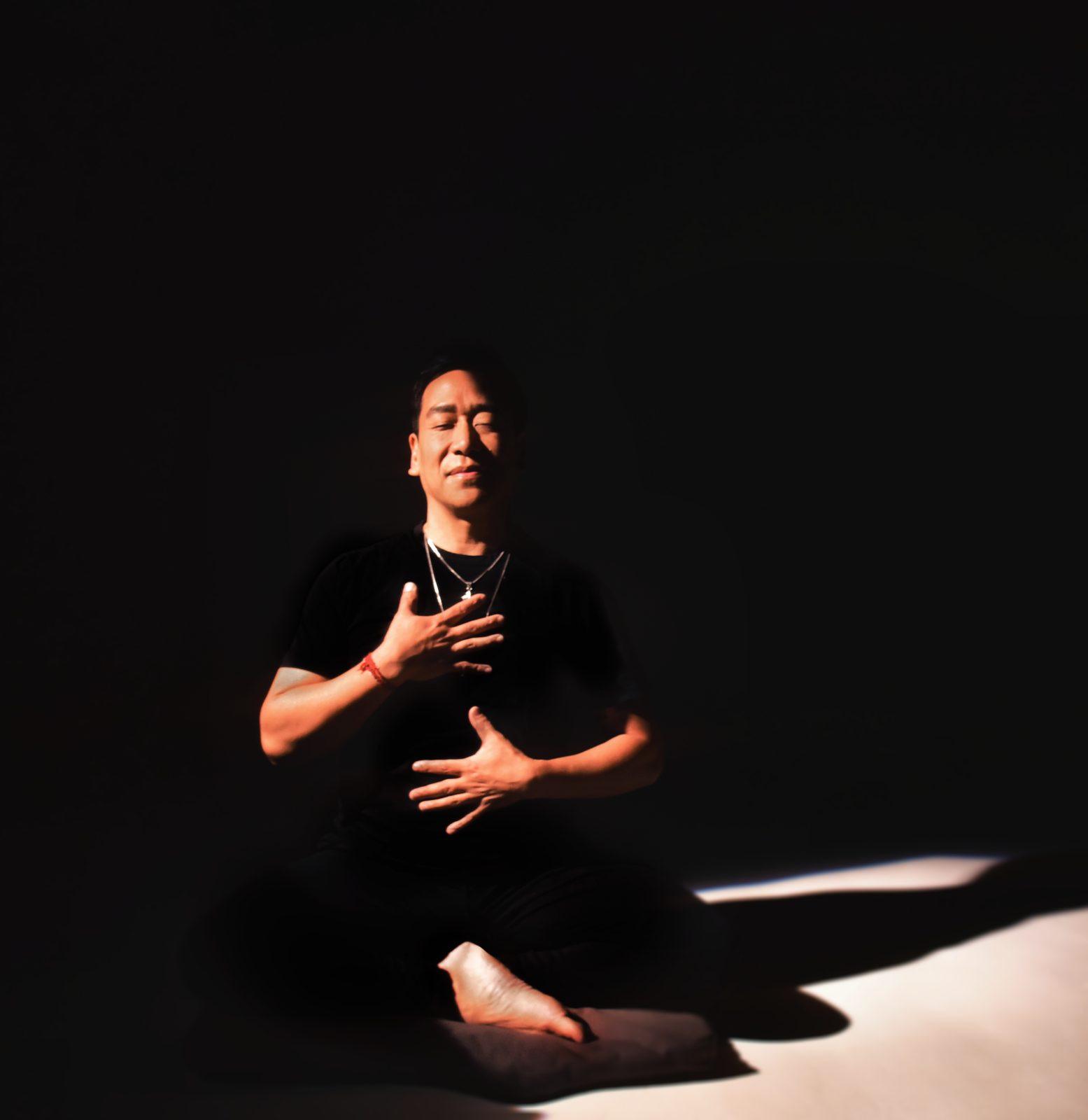 Ian Pai seated in meditation with a hand on his chest